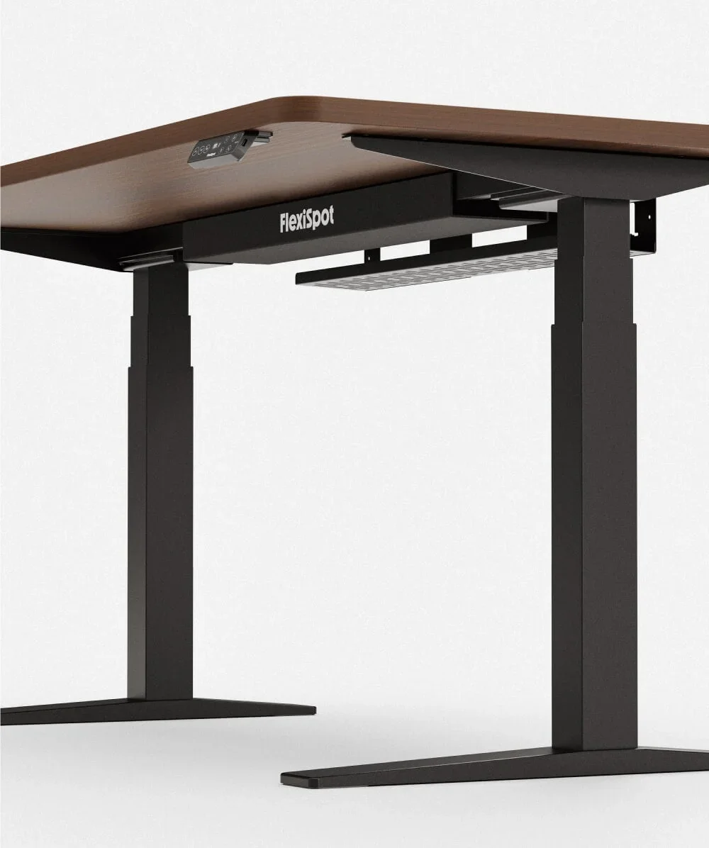 Three-quarter studio view of a walnut-top black C-frame desk corner showing the FlexiSpot-branded magnetic cable cover and mesh tray.