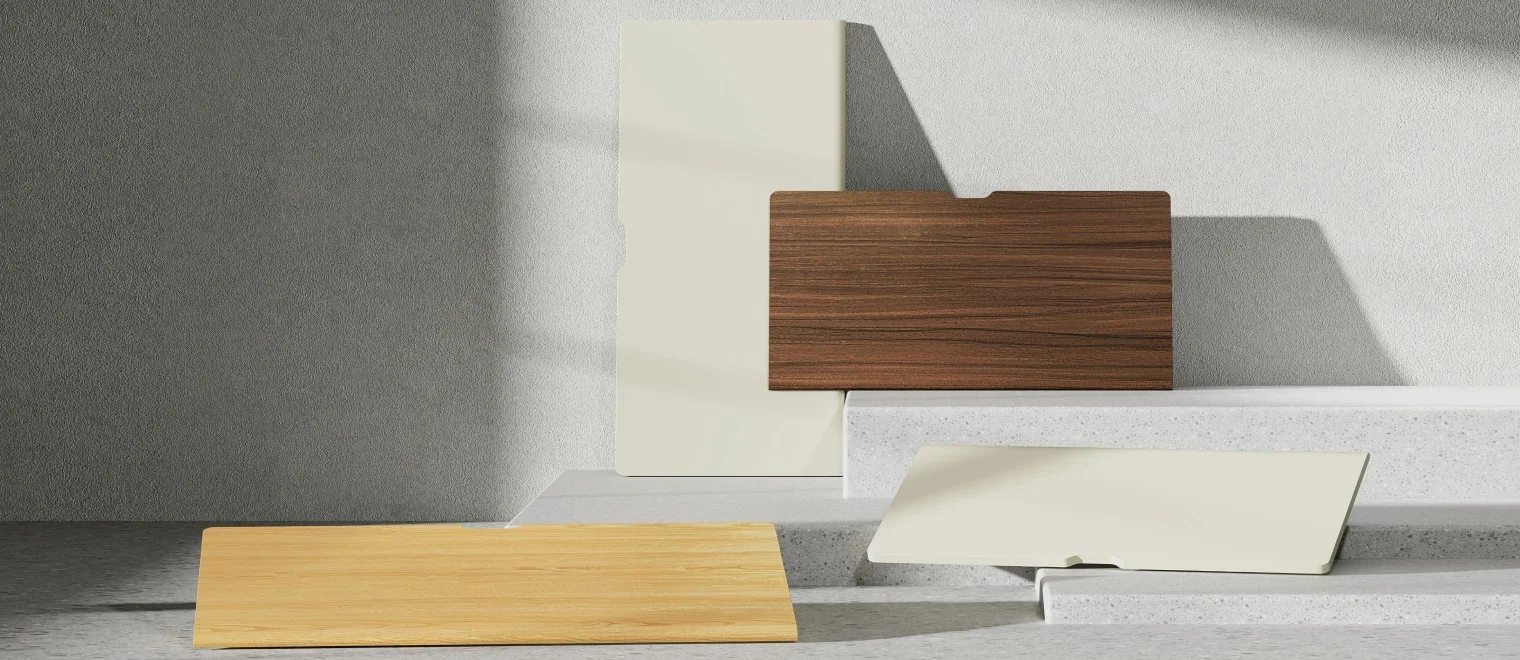 Curved-edge MDF desktops in walnut, cream and bamboo-look finishes on stone plinths in a grey studio.