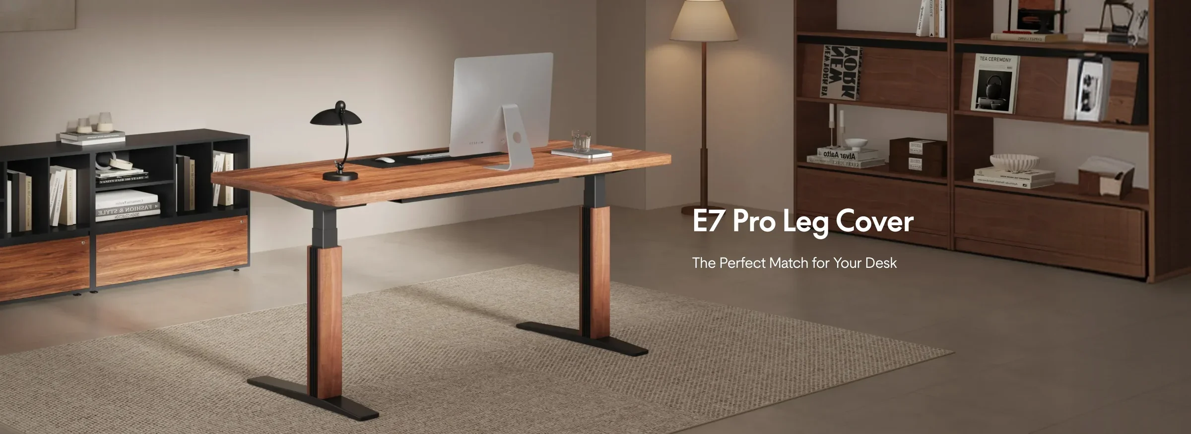 Wide banner of an E7 Pro with a walnut top and walnut leg covers in a warm living-room study with an iMac, desk lamp and shelving, with the product name and a tagline on the right.