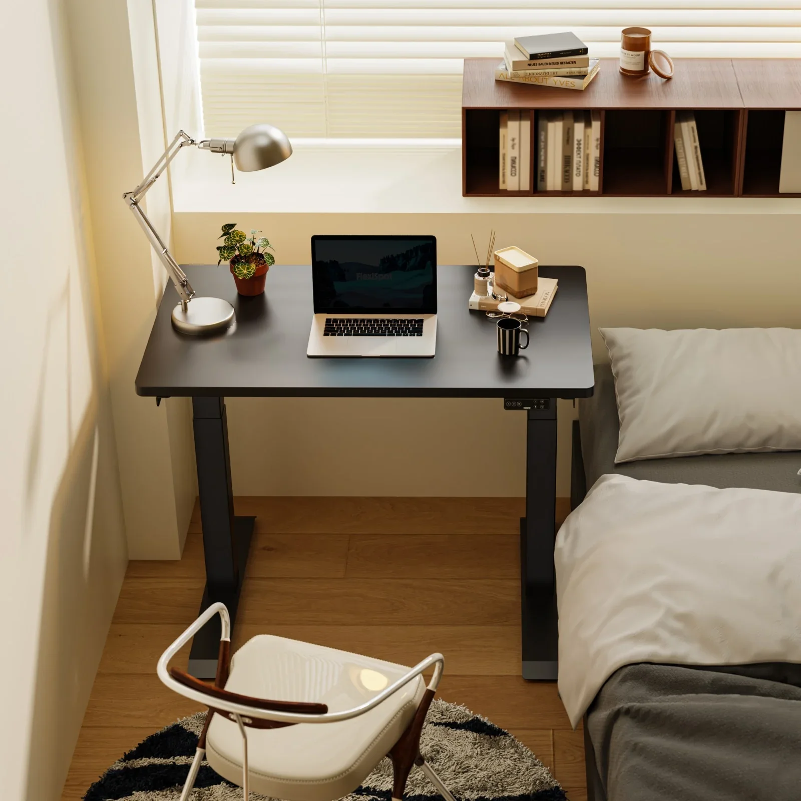 Black-frame E7 Mini with a black top beside a bed under a window with blinds, holding a laptop, desk lamp and plant, with a wall shelf above.