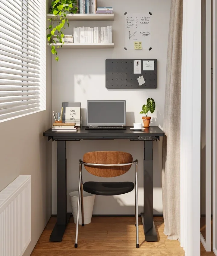 Black-frame compact desk with a black top in a bright window nook with pinboard and shelf.