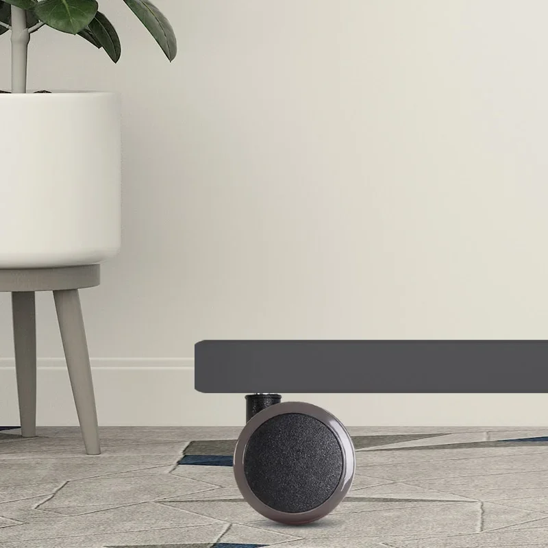 Caster fitted under a grey desk foot on a stone-tile floor beside a potted plant.