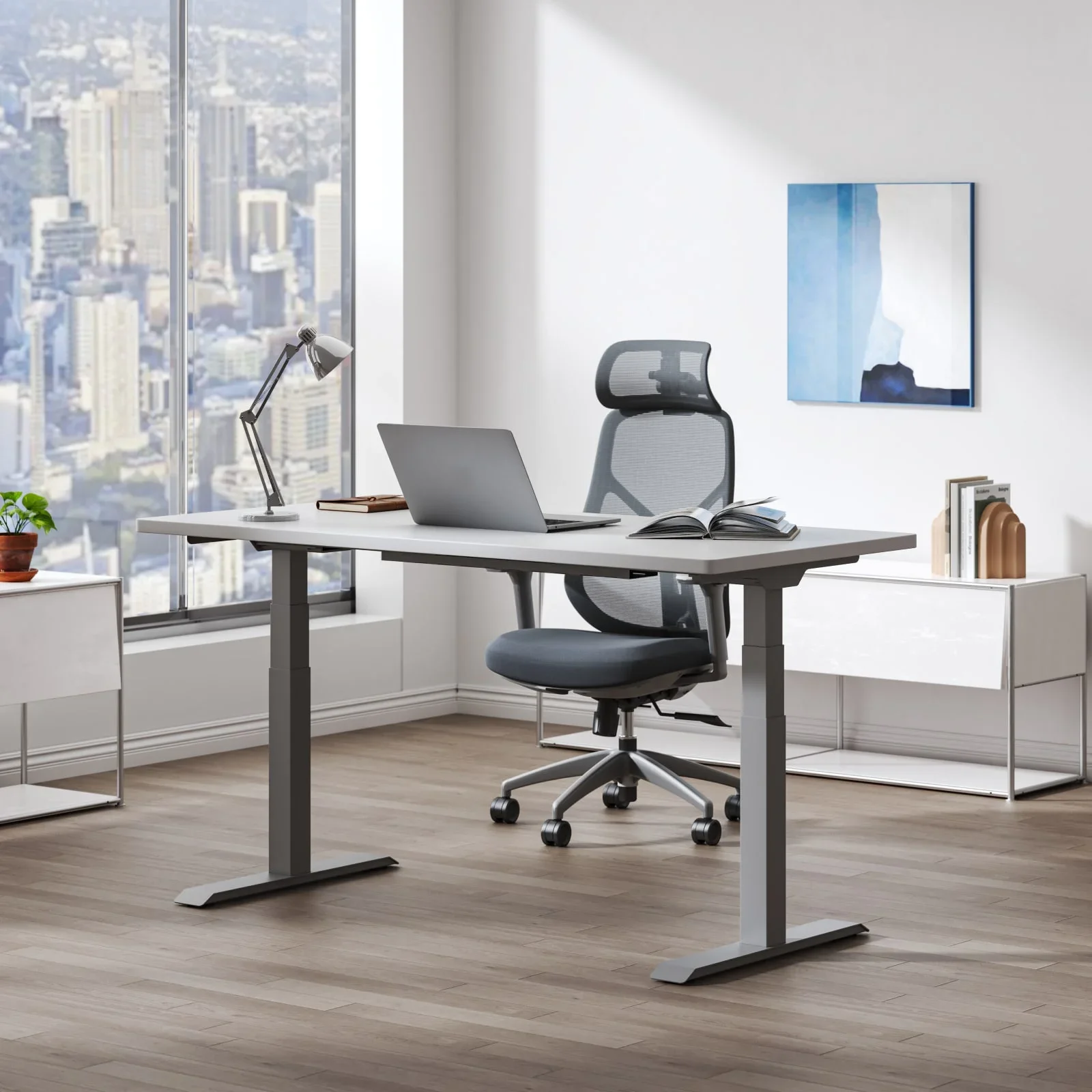 Grey-frame E7 with light grey top in a bright high-rise office with city view, laptop, lamp and grey mesh chair.