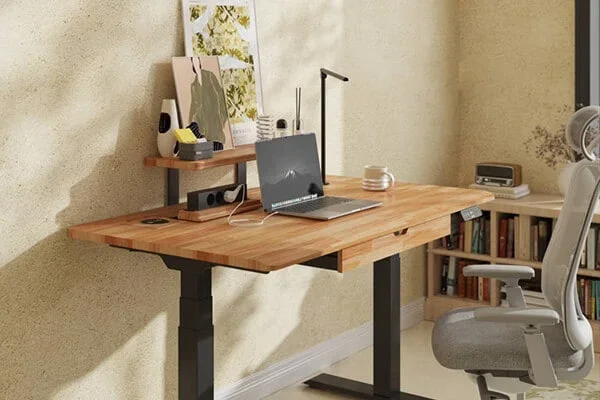Black-frame desk with a solid wood top, drawer and shelf riser, laptop and grey chair against a textured wall.