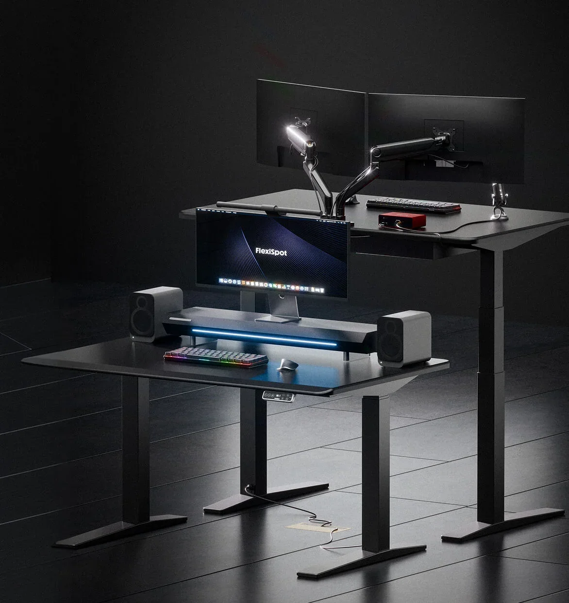 Dark studio render of two black desks, one at sitting height with a riser and one standing with dual monitor arms.