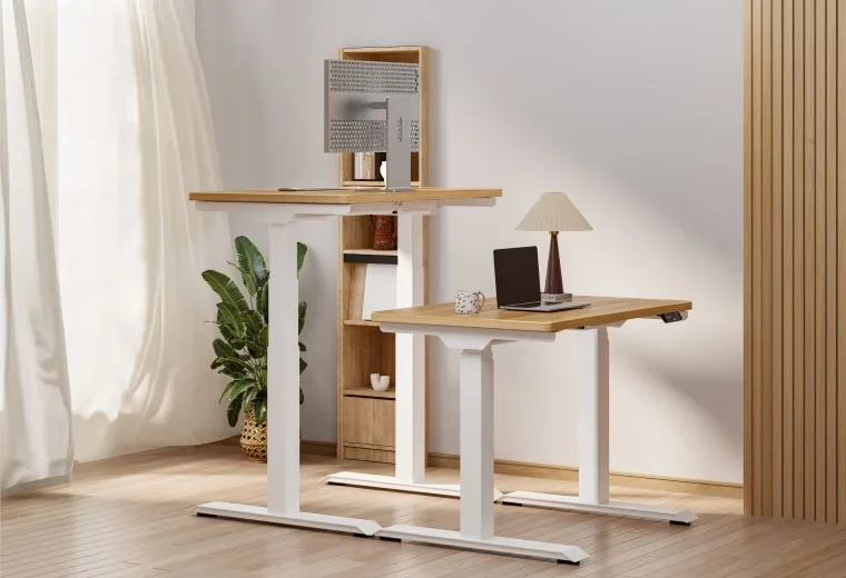 Two white-frame E7 Mini desks with light oak tops, one at standing height with a monitor and one at sitting height with a laptop and lamp, beside a wooden shelf.