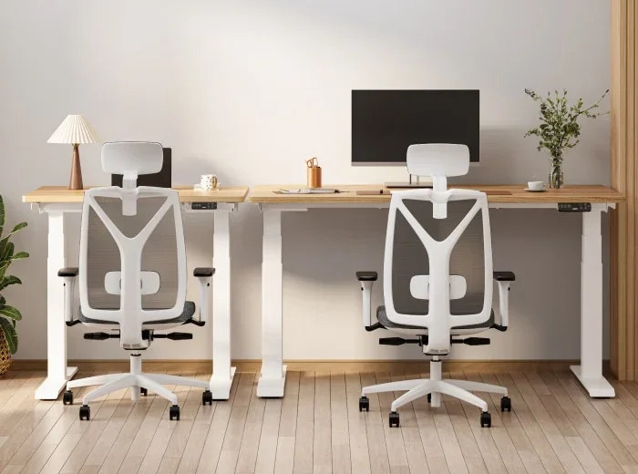 Two white-frame E7 Mini desks with light oak tops placed end to end, each with a white mesh ergonomic chair, one with a monitor and one with a lamp.