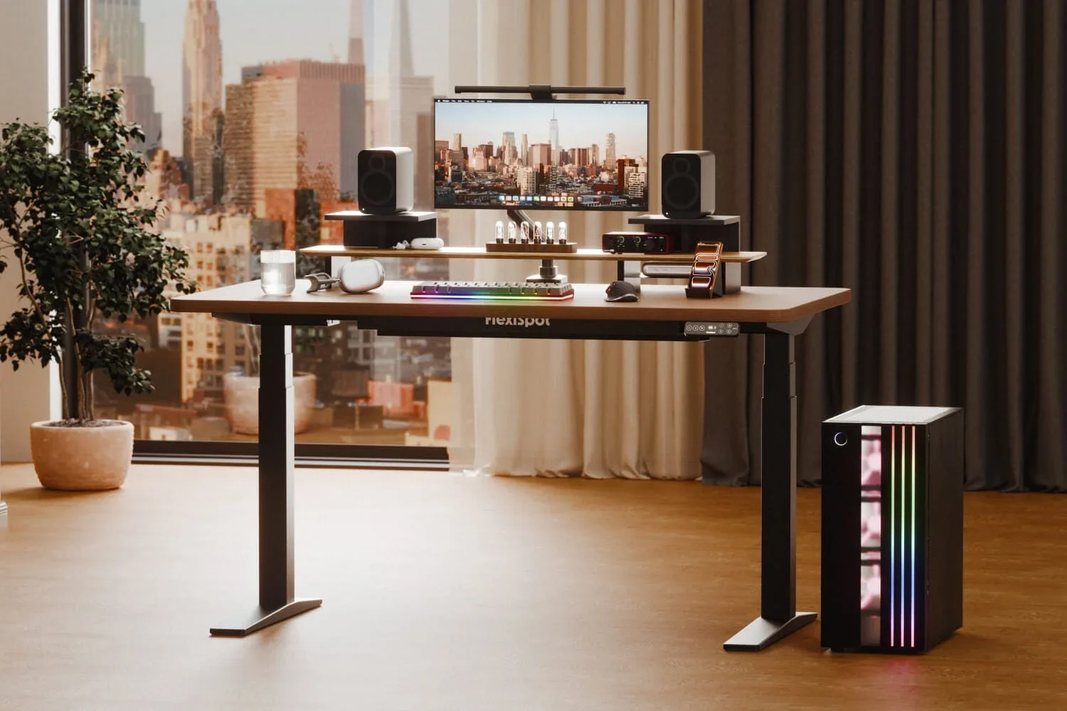 Black-frame walnut desk with FlexiSpot-branded cable cover, monitor on a riser, RGB keyboard, speakers and RGB PC tower in front of a city window; no marketing text.