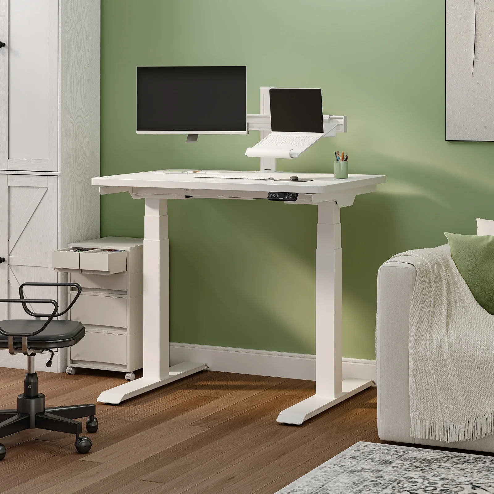 White-frame E7 Mini with a white top against a sage green wall, with a monitor on an arm, laptop stand, mobile drawer unit, office chair and sofa.