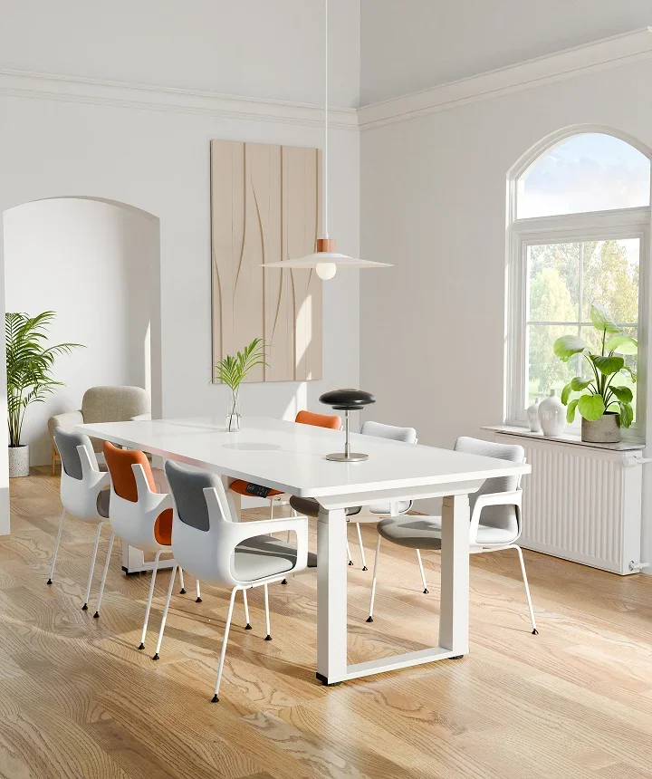 White-frame E7 Plus Max with a white top used as a long dining/meeting table with grey and orange chairs in a bright arched-window room.