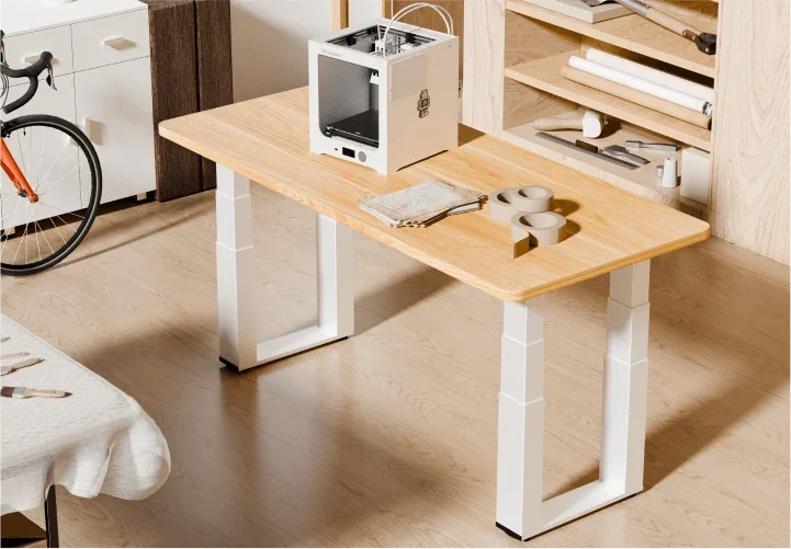 White-frame E7 Plus Max with a light oak top holding a 3D printer in a workshop-style room with a bike and shelves.