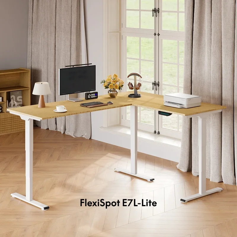White-frame E7L-Lite with a light wood L-shaped top in a bright room with tall windows, holding a monitor, printer, lamp and clock, with product-name text at the bottom.