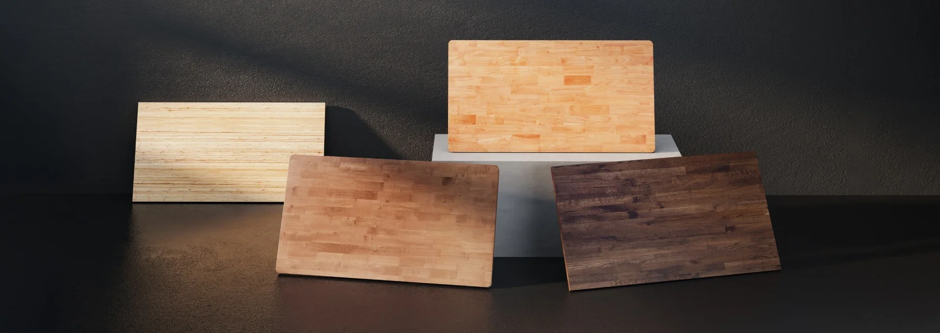 Wide dark studio shot of four butcher-block style wooden desktops in light to dark finishes propped against each other.
